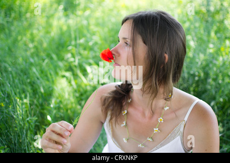 Une belle jeune femme est titulaire d'un coquelicot pour son nez, assis dans un pré Banque D'Images