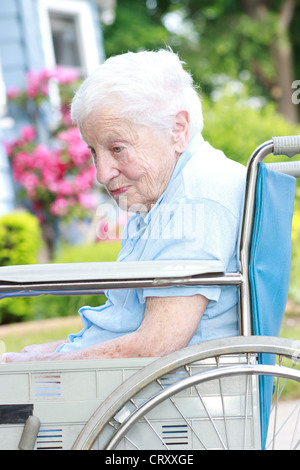 La haute dame en fauteuil roulant en face de la maison avec des fleurs roses Banque D'Images