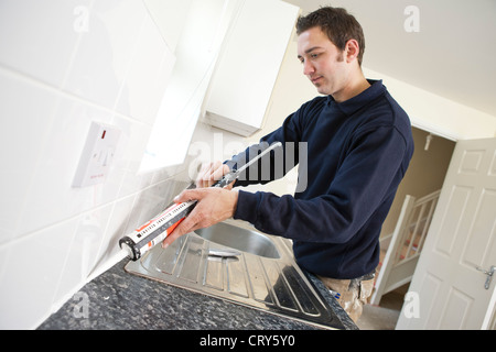 Builder s'applique de la pâte à tuiles autour d'un évier de cuisine Banque D'Images