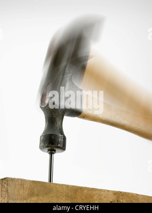 Un flou hammer hitting un clou dans un morceau de bois vu de légèrement en dessous, marteau reposant sur tête. Banque D'Images