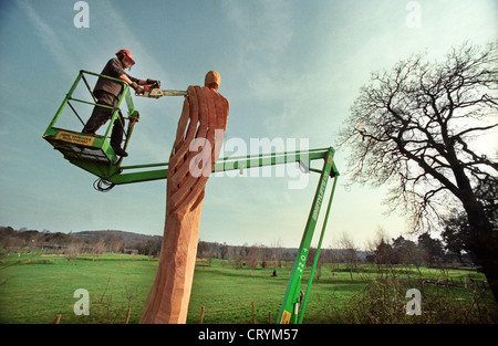 Un sculpteur à la tronçonneuse sur la plate-forme d'une sculpture cherrypicker un treillis figure à partir d'un chêne mort dans Broadwater Park, Godalming, Surrey, Angleterre, Royaume-Uni. Banque D'Images