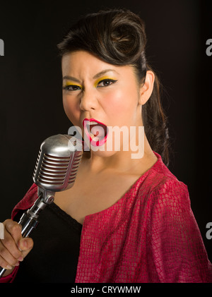 Asian girl singing into a microphone Shure style Elvis traditionnels Banque D'Images