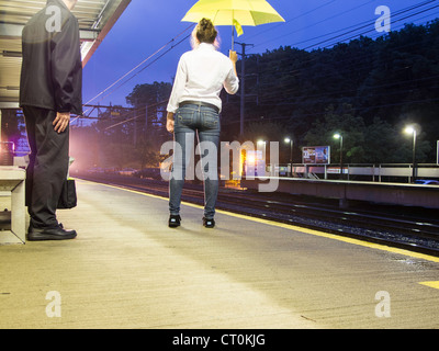 Les voyageurs attendent d'arriver à bord d'un train de voyageurs dans la rai sous un Brolly , Gare de banlieue, Riverside, CT Banque D'Images