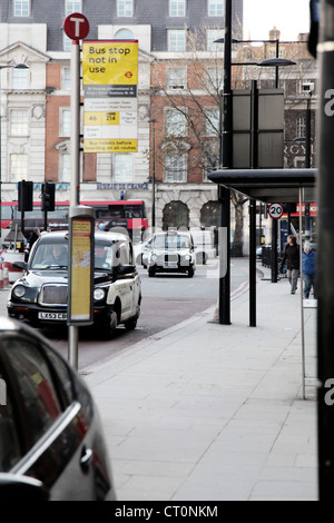 C'est une photo d'un arrêt de bus dans la rue de Londres. Nous pouvons voir les taxis et les bus à double étage sur les routes. Banque D'Images