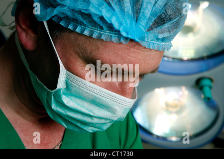 Un chirurgien masqué qui peut accueillir une unnderneath lumière chirurgicale dans une salle d'opération. Banque D'Images