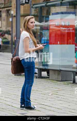 Portrait jeune femme blonde en attente à la gare routière de trains de banlieue avec Smartphone - Marktplatz Heilbronn Allemagne Europe Banque D'Images