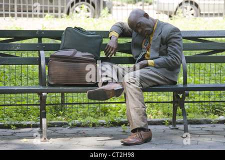 Homme fatigué avec ses affaires dort sur un banc de parc dans Central Park, New York City Banque D'Images