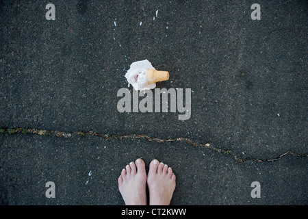 Pieds avec ice cream cone tombés sur la chaussée. Banque D'Images