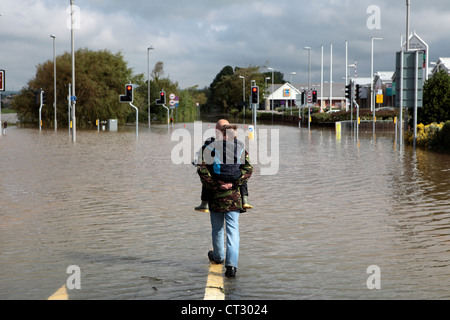 Un homme porte son fils et promenades à travers les routes inondées de Weymouth après des pluies torrentielles dans le Dorset Banque D'Images