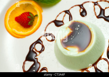 Panna cotta à la menthe sur plaque blanche décorée de fraise et orange. Banque D'Images