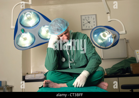 Un chirurgien assis sur une table d'opération, se reposer ses yeux. Banque D'Images