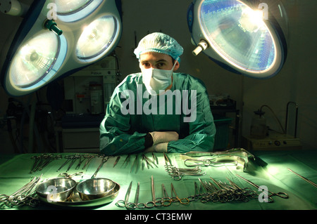 Un chirurgien masqués s'appuyant sur une table d'outils chirurgicaux stériles dans un théâtre de l'hôpital. Banque D'Images