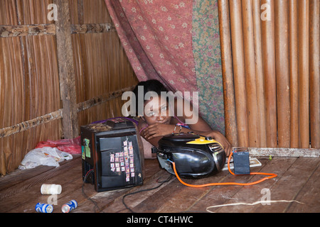 L'Indonésie, la Papouasie-Nouvelle-Guinée, Nuana Island. Woman resting in structure en bois par une télévision et une chaîne stéréo. Banque D'Images