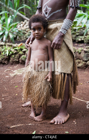 Pacifique Sud, Vanuatu, Port de l'IVL, Ekasup Village. Jeune garçon en costume traditionnel appuyé contre son père. Banque D'Images