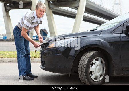 Pilote russe Senior essayant d'ouvrir le capot du compartiment moteur standing in front of car Banque D'Images