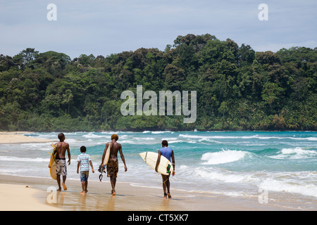 Surfers marche le long de la mer à la plage de l'Assistant (première plage) sur Isla Bastimentos, Bocas del Toro, PANAMA. Banque D'Images