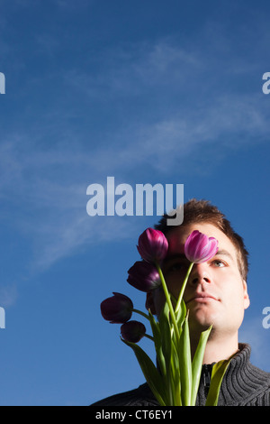Young man with pink tulip flowers against blue sky Banque D'Images