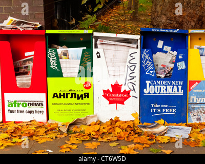 Ligne d'un journal gratuit et des distributeurs de magazines au centre de Londres Angleterre Royaume-uni avec les feuilles d'automne sur le terrain Banque D'Images