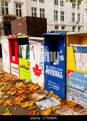 Ligne d'un journal gratuit et des distributeurs de magazines au centre de Londres Angleterre Royaume-uni avec les feuilles d'automne sur le terrain Banque D'Images