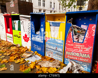 Ligne d'un journal gratuit et des distributeurs de magazines au centre de Londres Angleterre Royaume-uni avec les feuilles d'automne sur le terrain Banque D'Images