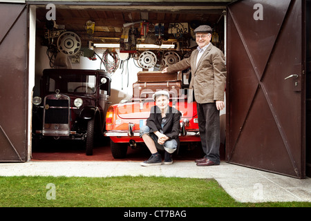 Grand-père et petit-fils avec voiture d'époque et le tronc valises en garage Banque D'Images