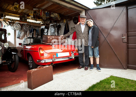 Grand-père et petit-fils avec voiture d'époque et le tronc valises en garage Banque D'Images