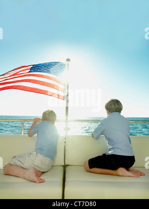Les garçons à l'arrière d'un yacht avec le drapeau américain, face à la mer Banque D'Images