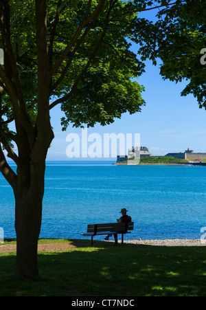 L'homme sur le banc à Queen's Royal Park sur le lac Ontario à Old Fort Niagara (USA) dans la distance, Niagara-on-the-Lake, Ontario, Canada Banque D'Images