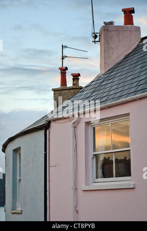 Reflet de coucher de soleil dans la fenêtre à guillotine d'une maison dans le port de Tenby, Pembrokeshire, aux antennes et seagull perché sur la cheminée. Banque D'Images