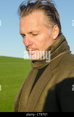 Une pensive et sombre à l'homme mature dans la quarantaine avec le chaume à la recherche vers le bas. Il porte un foulard vert et veste. Banque D'Images