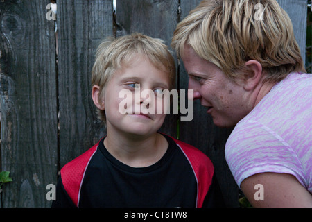 Garçon de dix ans d'oeil douteux que mom chuchote quelque chose à son oreille. Banque D'Images