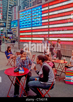 Les gens se détendre à tables à Times Square, New York City. En arrière-plan est le drapeau des États-Unis. Banque D'Images