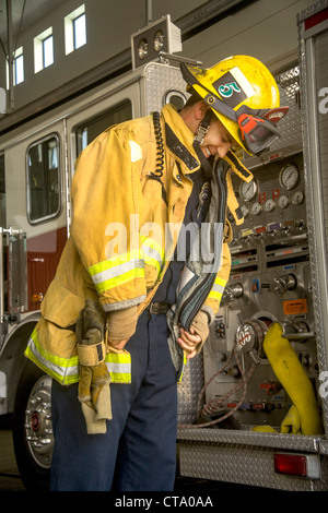 Porter son casque, un jeune pompier enfile sa veste de sécurité jaune à une caserne de Laguna Niguel, CA. Banque D'Images