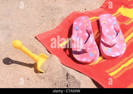 Pelle en plastique jaune dans la plage avec sable pour enfants cute pink flip flop sandals sur une serviette colorée Banque D'Images