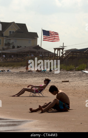 Les touristes à prendre le soleil sur la plage de Surf City Topsail Island , , CAROLINE DU NORD , USA avec stars and stripes drapeau Américain Banque D'Images