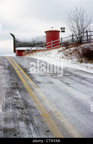 Une route couverte de neige avec une grange à l'arrière-plan. Banque D'Images