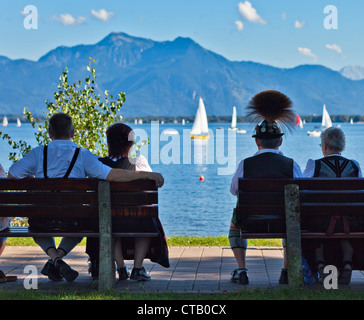 Des couples portant des vêtements traditionnels assis sur des bancs près de Harbour au lac de Chiemsee, Prien, Chiemgau, Haute-Bavière, Allemagne Banque D'Images
