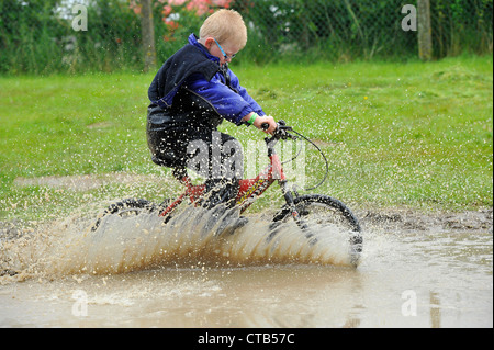 L'enfant sur une course de moto dans une flaque d'eau créant un splash. Banque D'Images