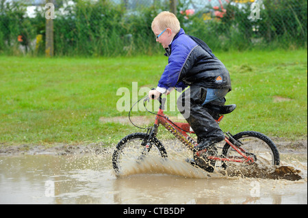 L'enfant sur une course de moto dans une flaque d'eau créant un splash. Banque D'Images