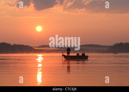 Pêcheur dans un bateau silhouetté contre un soleil levant. Banque D'Images