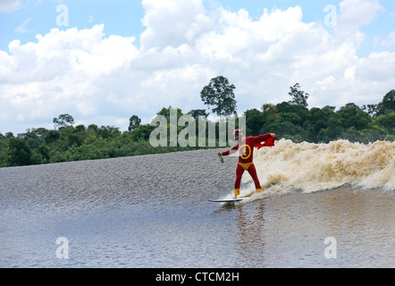 Homme étrange en costume de super-héro rouge river surf un mascaret vague sur la rivière Kampar, également connu sous le nom de Bono ou les 7 fantômes. Banque D'Images