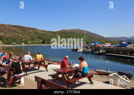 Les gens assis à des tables de pique-nique sur la mer avec le Loch Broom port de pêche dans le nord-ouest de la côte des highlands en été. UK Ecosse Ullapool Banque D'Images