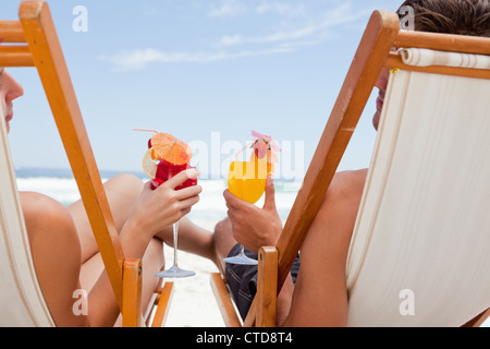 Vue arrière d'un jeune couple holding cocktails tout en restant assis sur leurs chaises longues Banque D'Images