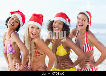 Quatre amis qui rient tout en mettant leurs mains sur leurs hanches, comme ils portent des Santa hats Banque D'Images