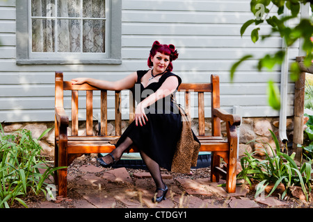 Style des années 1950 pinup model posing comme une femme au foyer, c'est assis sur un banc Banque D'Images