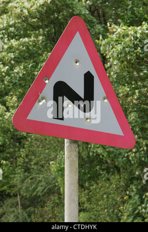 Un panneau routier britannique d'un double avertissement à venir. bend Celui-ci en milieu rural a été tué à Dorset et parsemé de trous de balle. Angleterre, Royaume-Uni. Banque D'Images