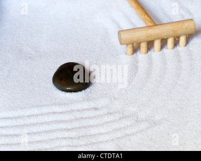 Close-up of a un jardin zen japonais avec un râteau en bois et une pierre noire. Banque D'Images