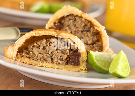 Snack-péruvien appelé Empanada (PIE) rempli de viande de boeuf haché, l'oignon, le raisin sur la plaque avec les limes Banque D'Images