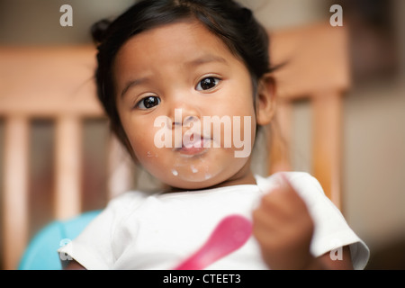 Hispanic baby girl apprendre à mort par elle-même avec du lait renversé sur sa bouche Banque D'Images