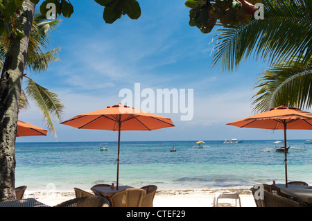 Table et chaises sous un parapluie orange sur une plage de sable blanc Banque D'Images